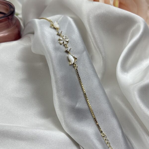 Pozlaćena srebrna narukvica sa motivima leptira od sedefa i cirkonima na bijeloj satenskoj podlozi